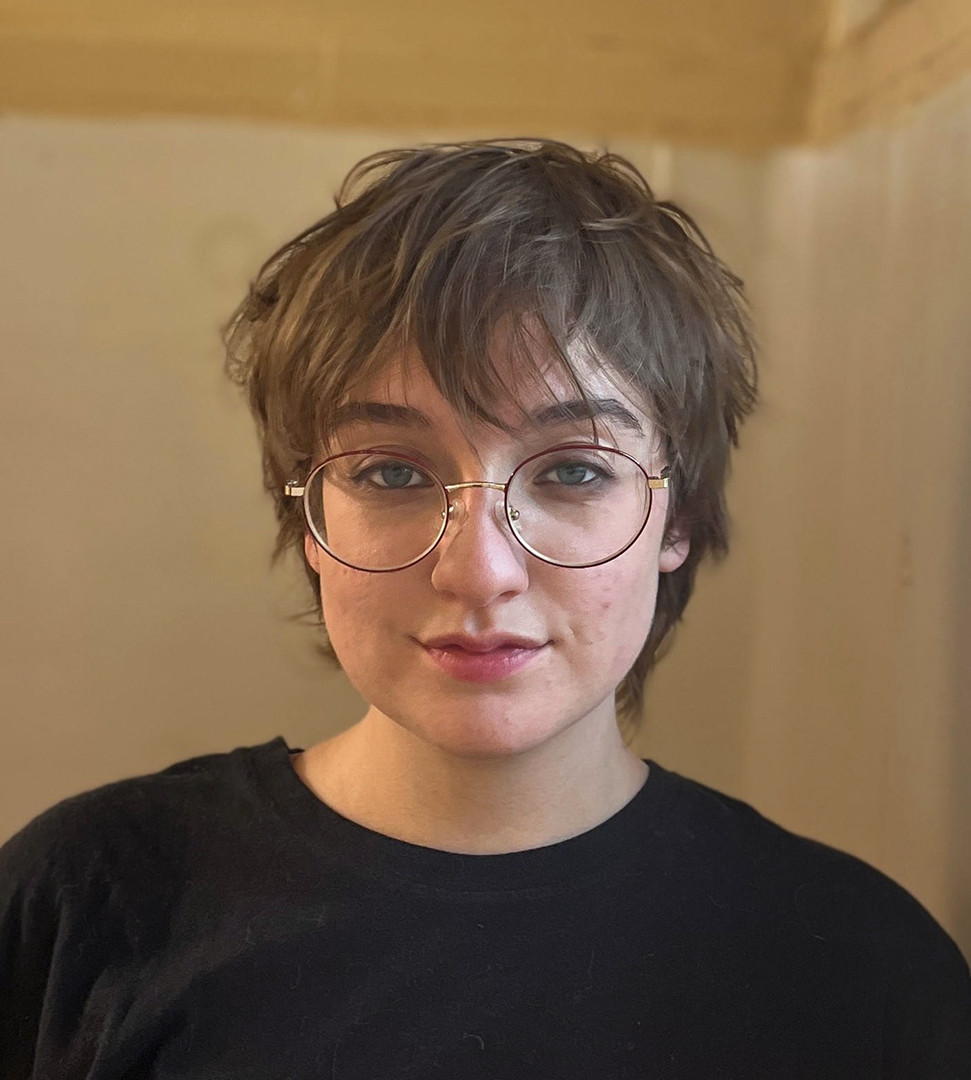 Young person with short blond hair, glasses, wearing a black shirt